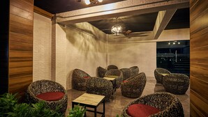 Un espacio lounge moderno con sillas tejidas únicas y una mesita pequeña, que cuenta con un ventilador de techo e iluminación ambiental.