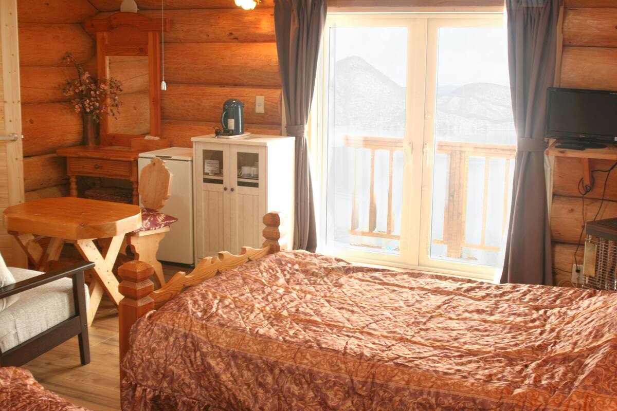 A wooden cabin room with a bed, a wooden table, a small cabinet, and a television.