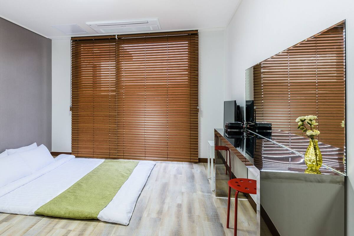 A hotel room with a bed, a desk with a chair, a television, and a window with blinds.