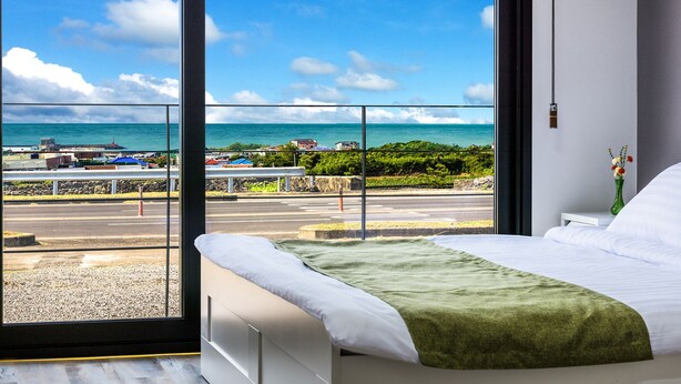 Habitación de hotel con un amplio ventanal que ofrece vistas al mar y a una carretera.