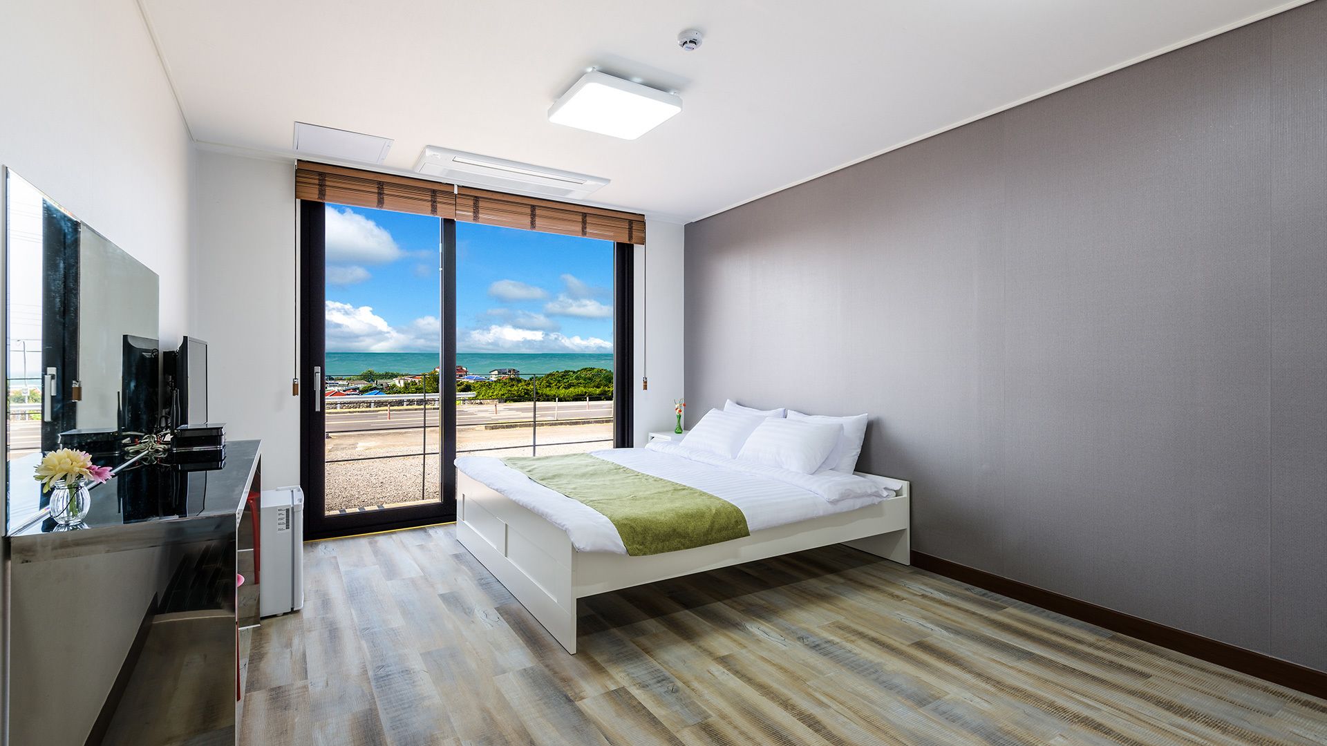 Ett modernt hotellrum med en säng, ett skrivbord och ett stort fönster med utsikt över havet.