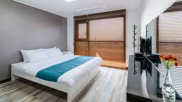 Moderni hotellihuone, jossa on suuri sänky, puusälekaihtimet, taulutelevisio ja maljakko, jossa on kukkia.