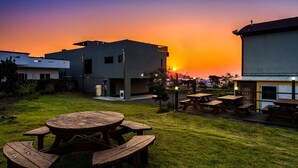 Un edificio moderno con techo plano y un amplio patio con mesas de picnic de madera.