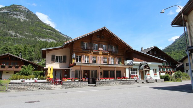 Ein traditionelles Holzhaus mit Balkon, einem Schild mit der Aufschrift 'Ritzl's Pub' und einer Bergbäckgrund.