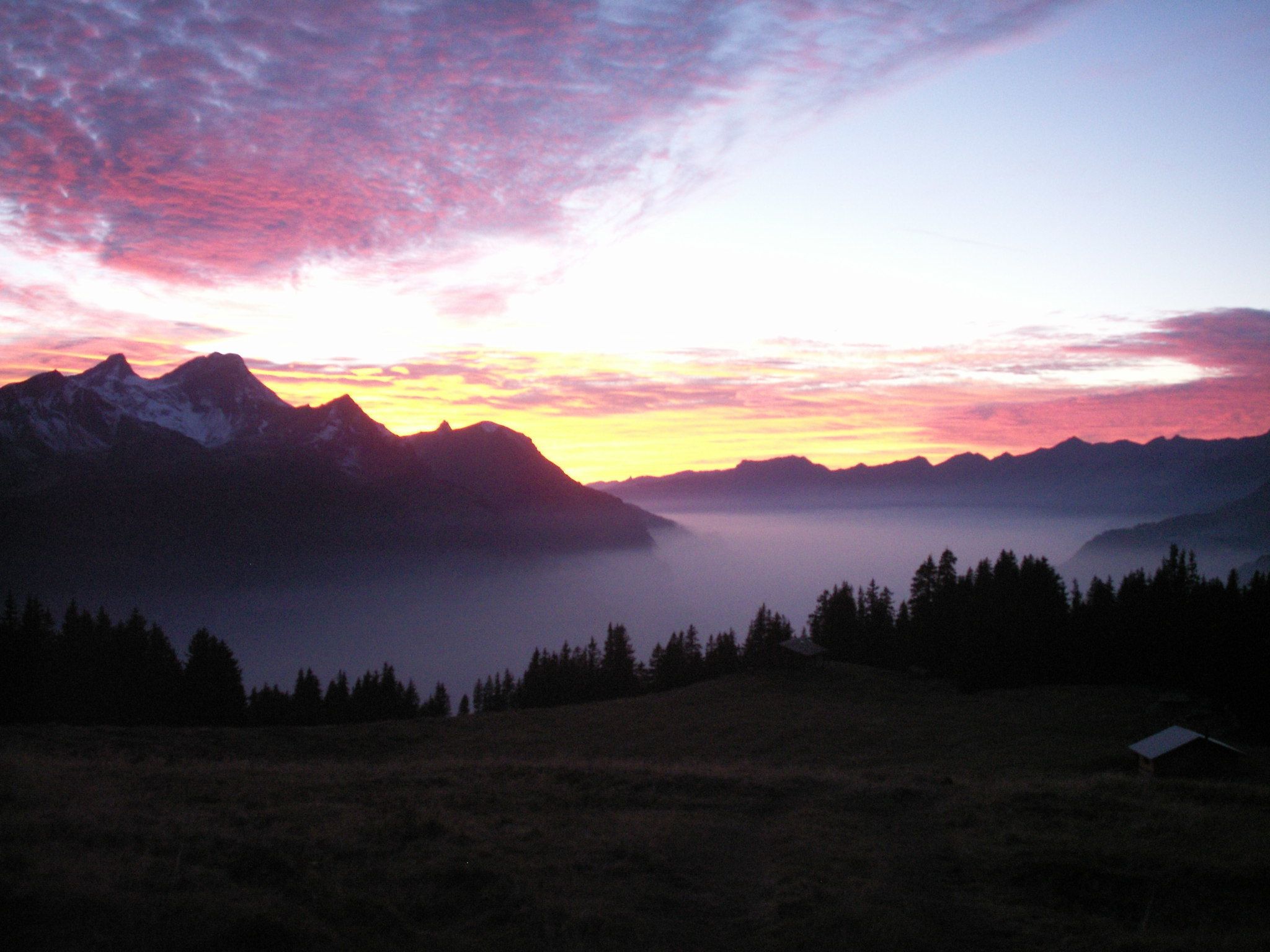 A mountainous landscape with a clear sky and a small cabin in the foreground.