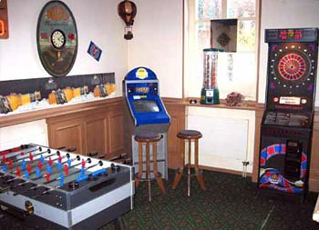 Una habitación con mesa de futbolín, dardos y un jukebox.