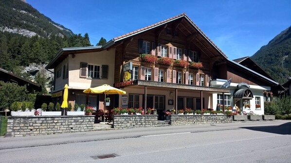 A traditional wooden building with a stone facade, a balcony with flowers, and a sign for a restaurant and pub. - Hotel Restaurant Alpina (Innertkirchen)