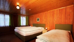 Ein Zimmer mit zwei Betten, Holzwänden, einem gerahmten Bild und einem Fenster mit Vorhängen.
