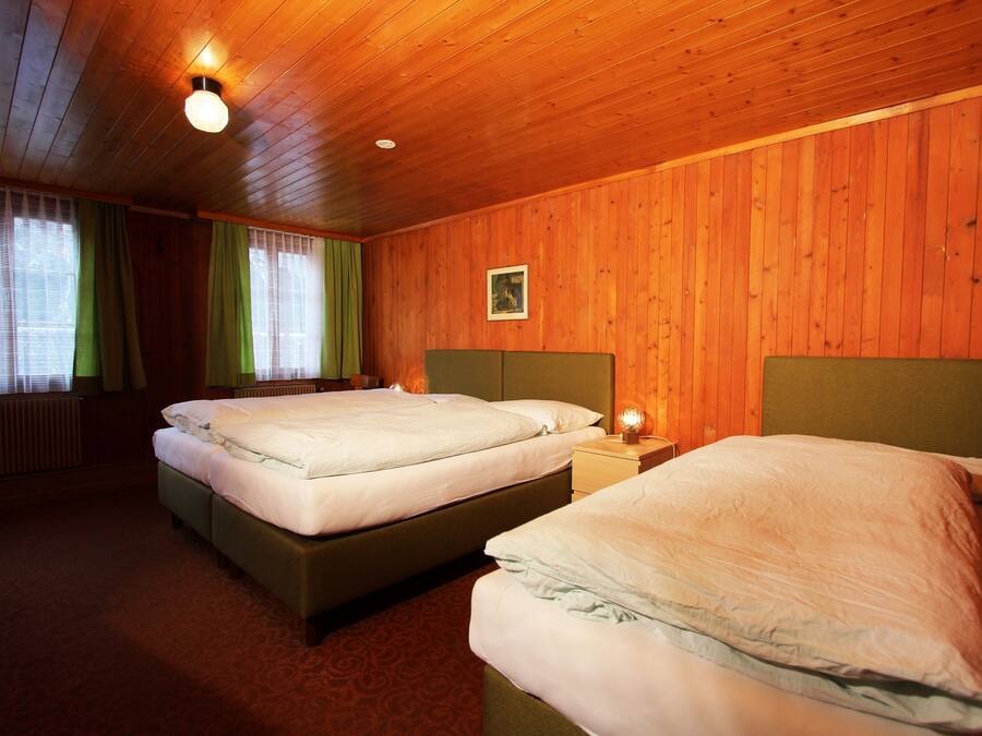 A room with two beds, wooden walls, a framed picture, and a window with curtains.