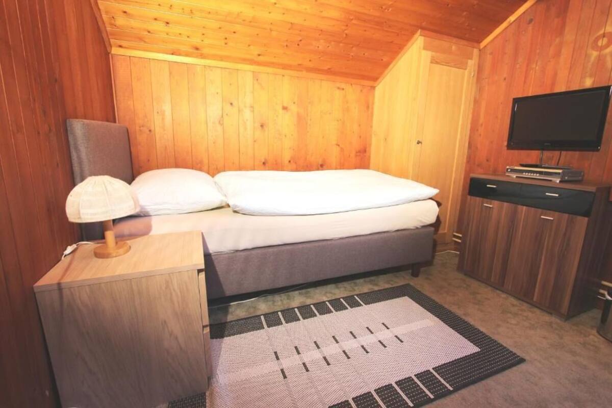 A wooden-paneled room with a bed, a television, and a desk with a lamp.