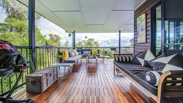 Una terraza techada al aire libre con piso de madera, un sofá, una mesa de comedor y una parrilla.