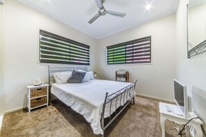 A bedroom with a bed, a nightstand, a TV on a stand, and a ceiling fan.