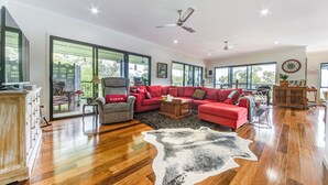 Amplia sala de estar con un sofá seccional rojo grande, un sillón gris y una mesa de centro de madera. Una ventana grande ofrece luz natural y vistas al exterior.