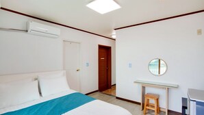 Une chambre d’hôtel équipée d’un lit, d’un bureau, d’un tabouret, d’un climatiseur, d’un miroir et d’une porte.