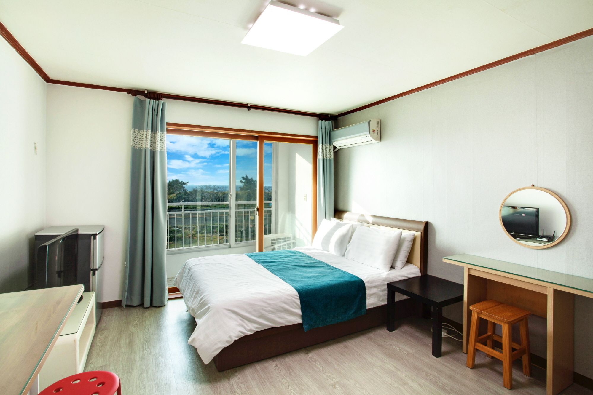 A hotel room with a bed, a desk, a chair, a TV, and a window with a view of the outdoors.