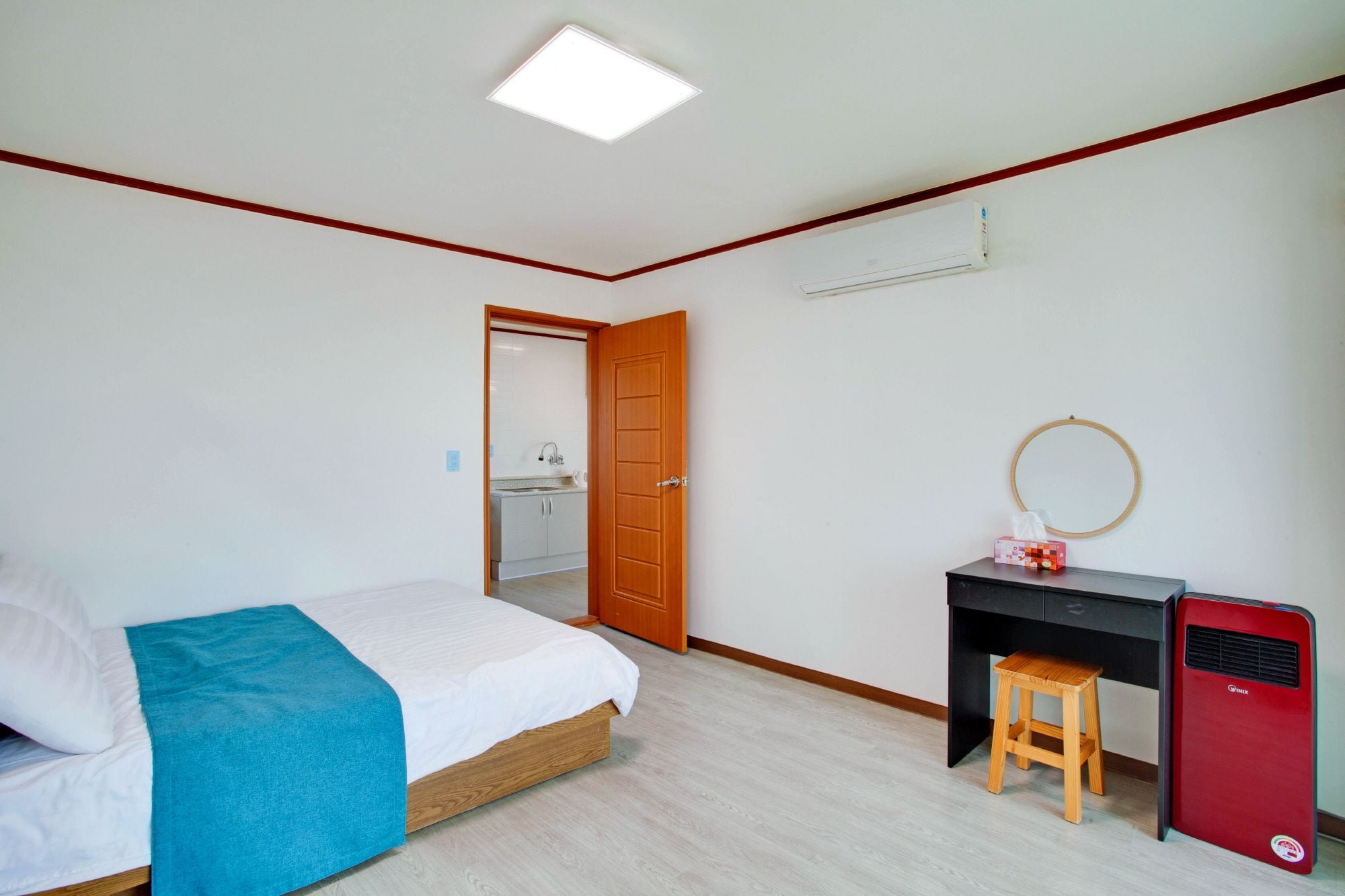 Een slaapkamer met een bed, een bureau, een krukje, een verwarming en een spiegel.