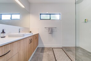 A modern bathroom with a wooden vanity, a large mirror, a small window, and a glass shower enclosure.