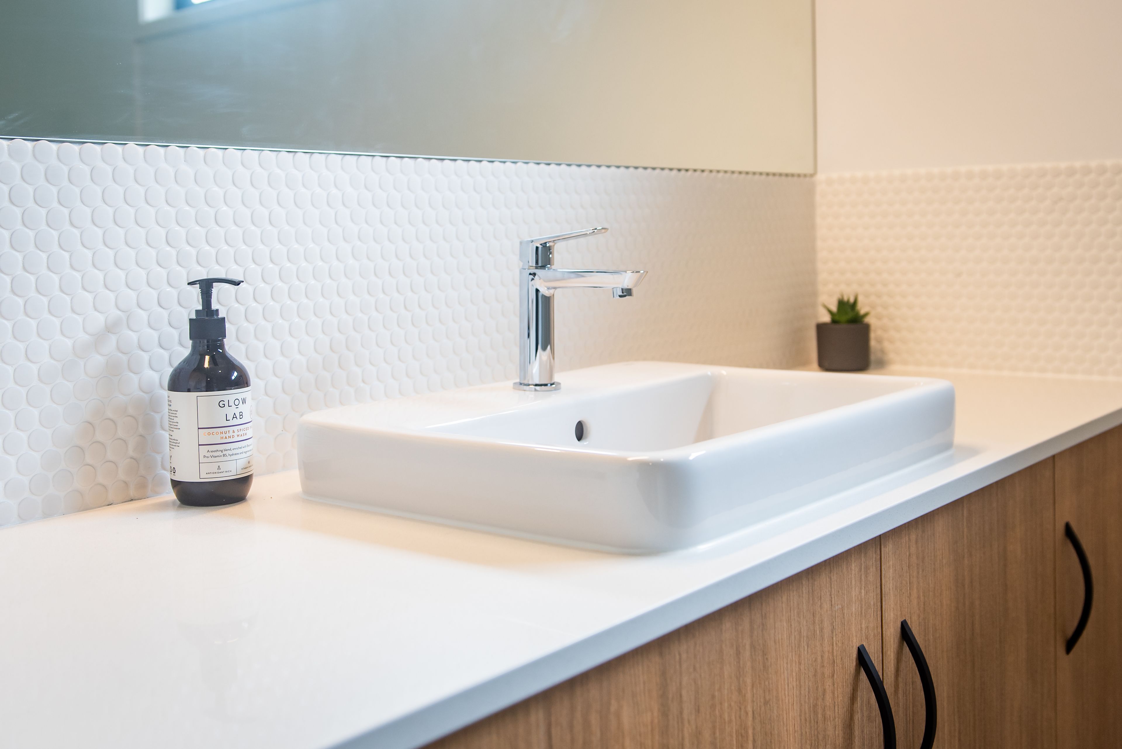 A bathroom with a white sink, a mirror, and a bottle of hand sanitizer.