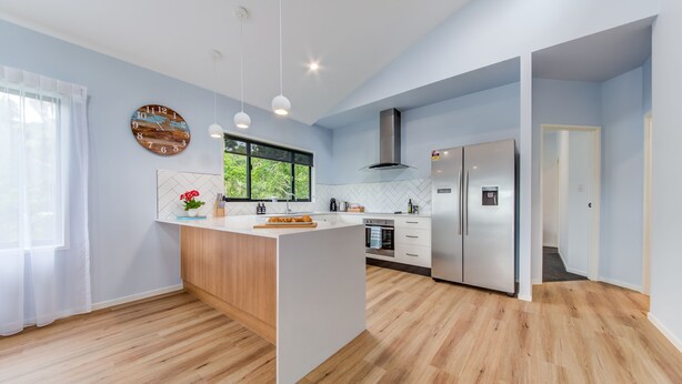 A modern kitchen with a central island, wooden flooring, and a large window.