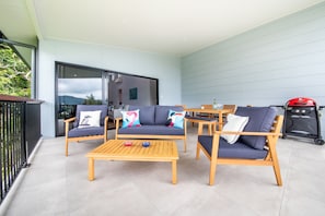 Relax in this serene outdoor space with a sofa, armchairs, and coffee table, surrounded by a glass door leading to a balcony with a view.