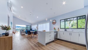 A modern kitchen with a large island, wooden flooring, and a view of greenery outside.