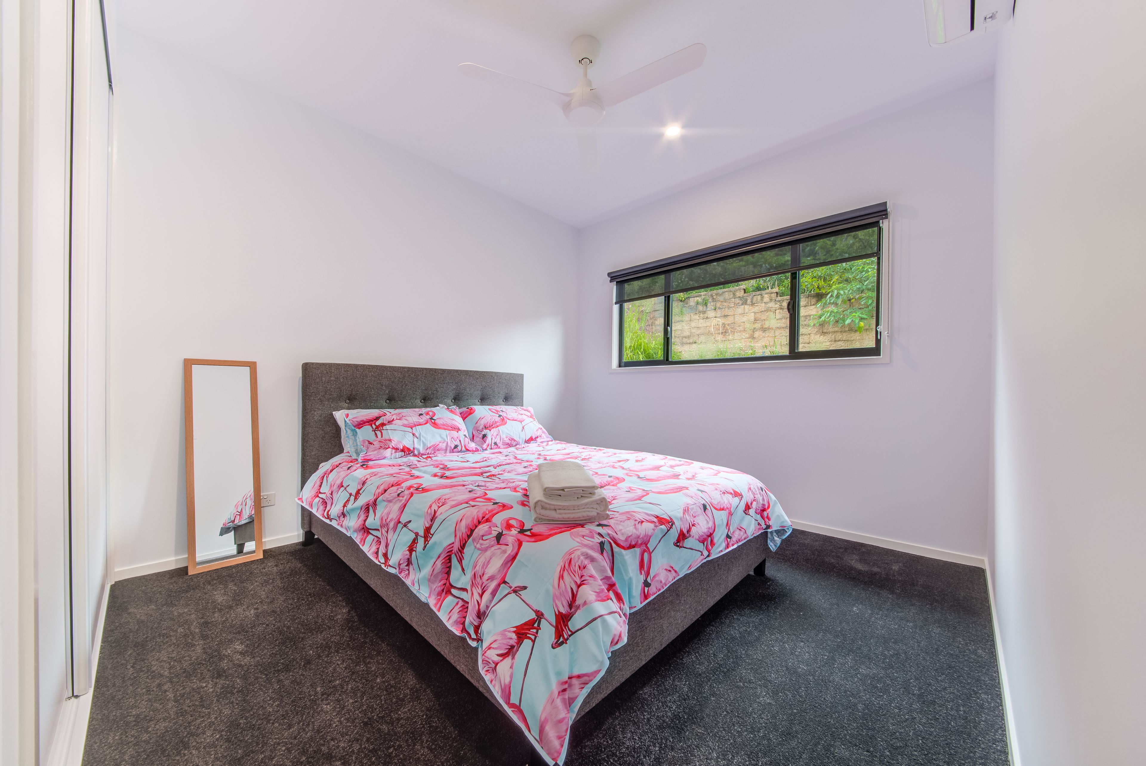 Un dormitorio con cama, ventana, ventilador de techo y espejo.