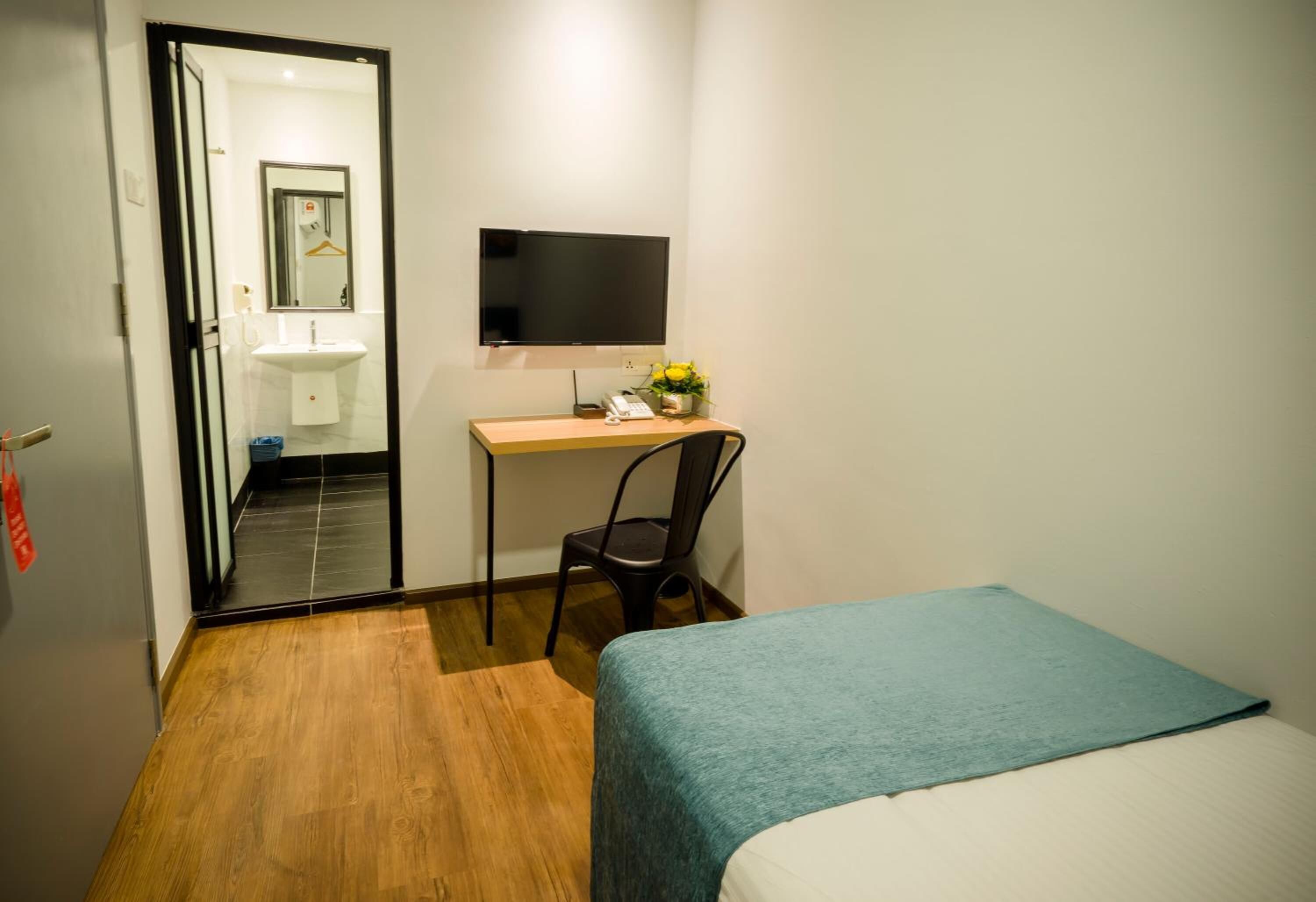 Une chambre d’hôtel comprenant un lit, un bureau avec une chaise, un téléviseur à écran plat, un miroir et une petite table sur laquelle est posé un vase de fleurs.