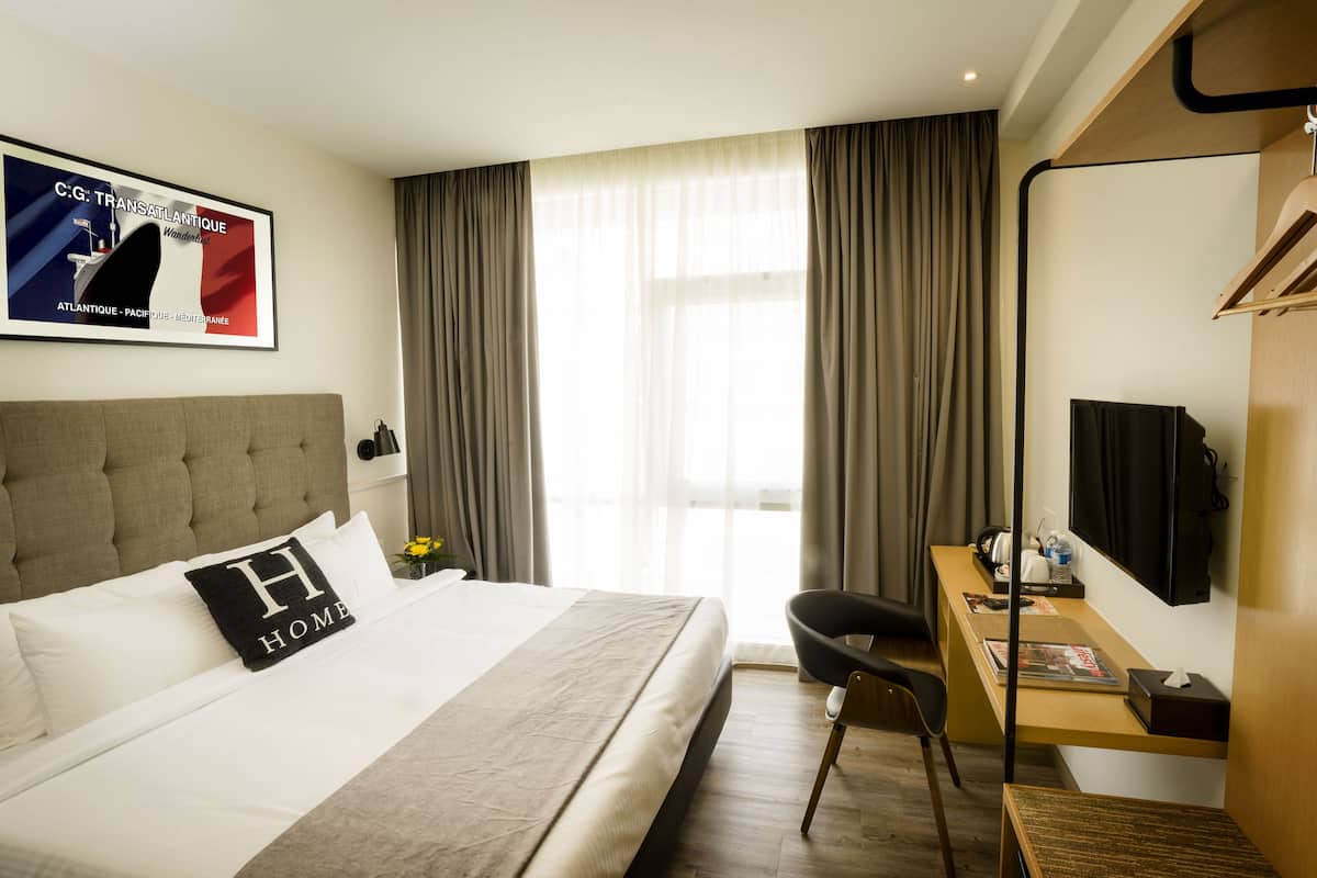 A hotel room with a large bed, a desk, a chair, a TV, and a window with curtains.