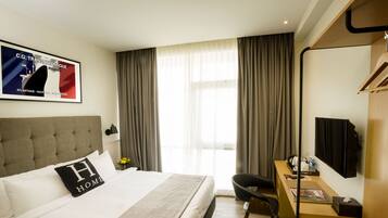 Habitación de hotel con una cama grande, un escritorio, una silla, un televisor y una ventana con cortinas.
