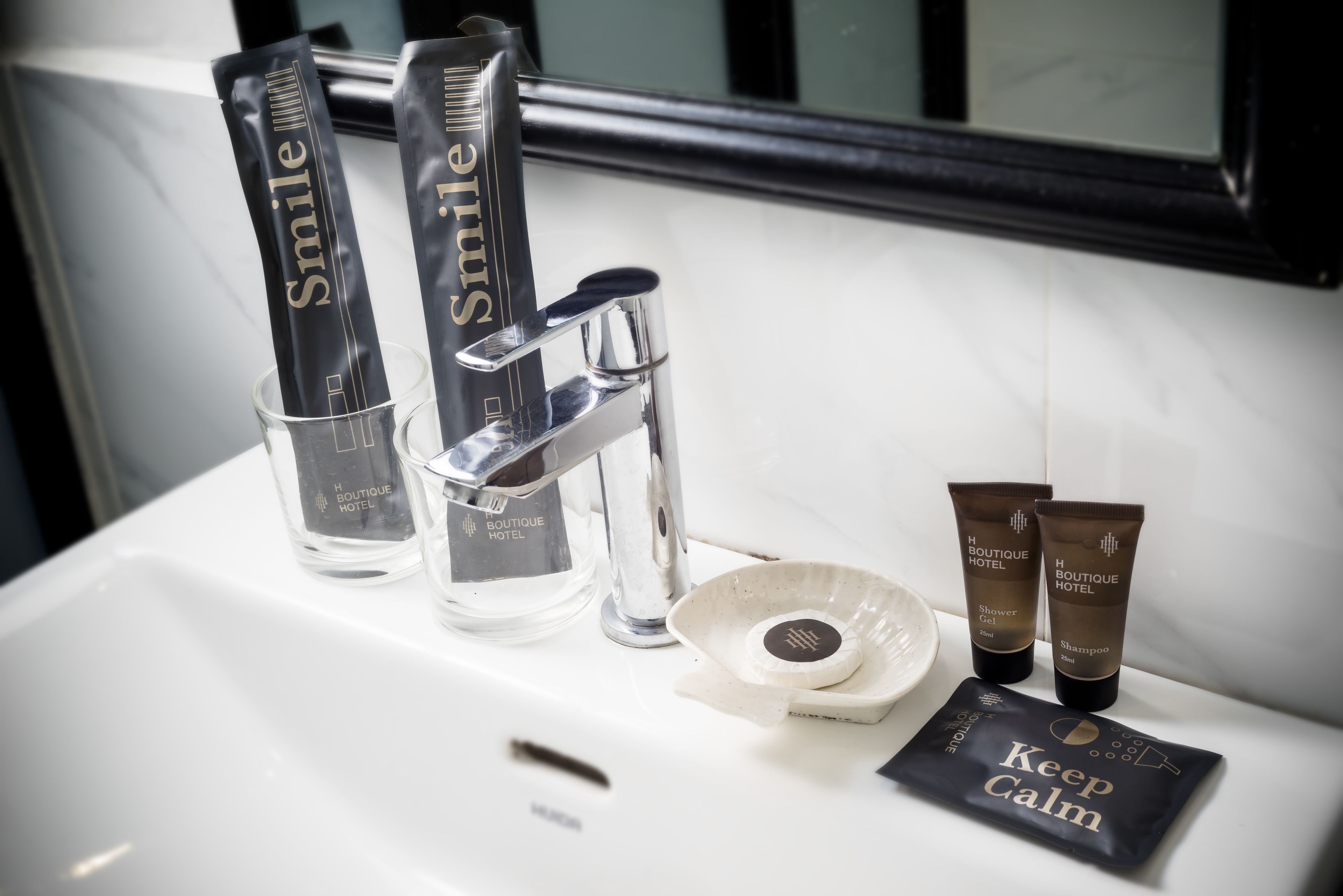 Un lavabo de bany amb productes de tocador, incloent una ampolla etiquetada com a "Smile", un tub de gel de dutxa, un tub de xampú i una targeta que diu "Keep Calm".