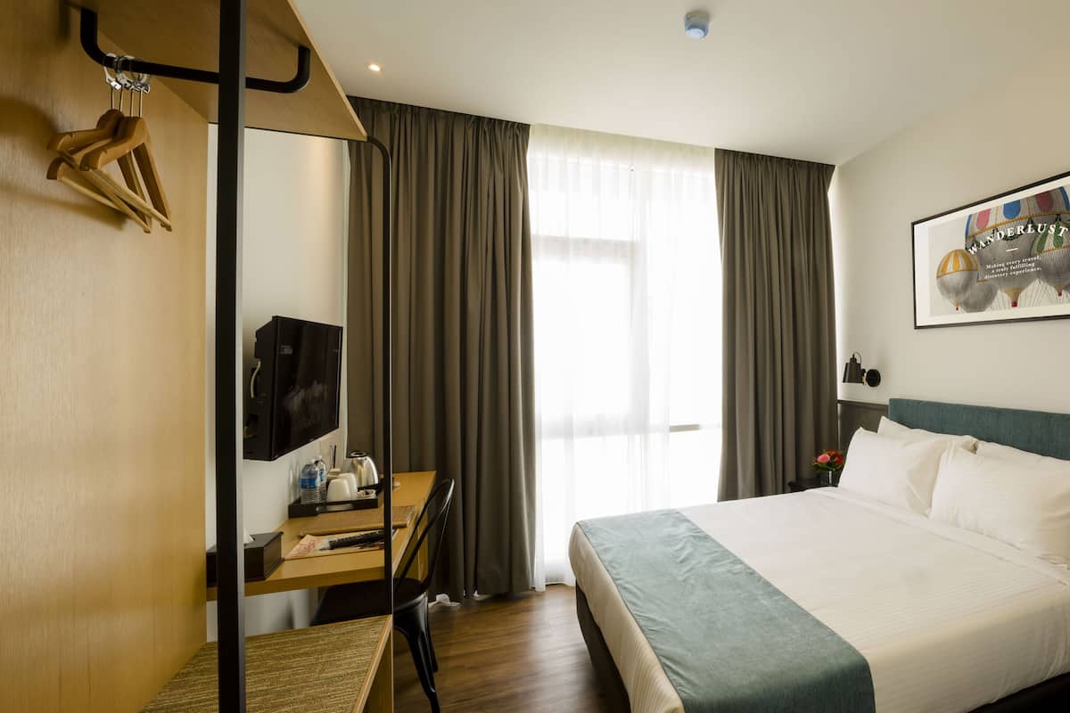 A hotel room with a bed, a desk with a chair, a television, and a window with curtains.