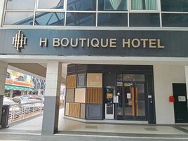 The exterior of H Boutique Hotel with a modern facade, a visible entrance, and a parking area in the background.