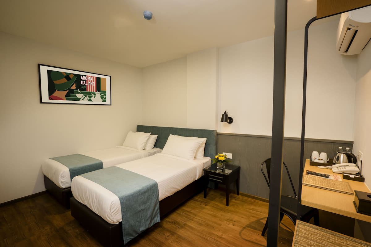 A hotel room with two beds, a desk with a telephone and a coffee maker, and a framed picture on the wall.