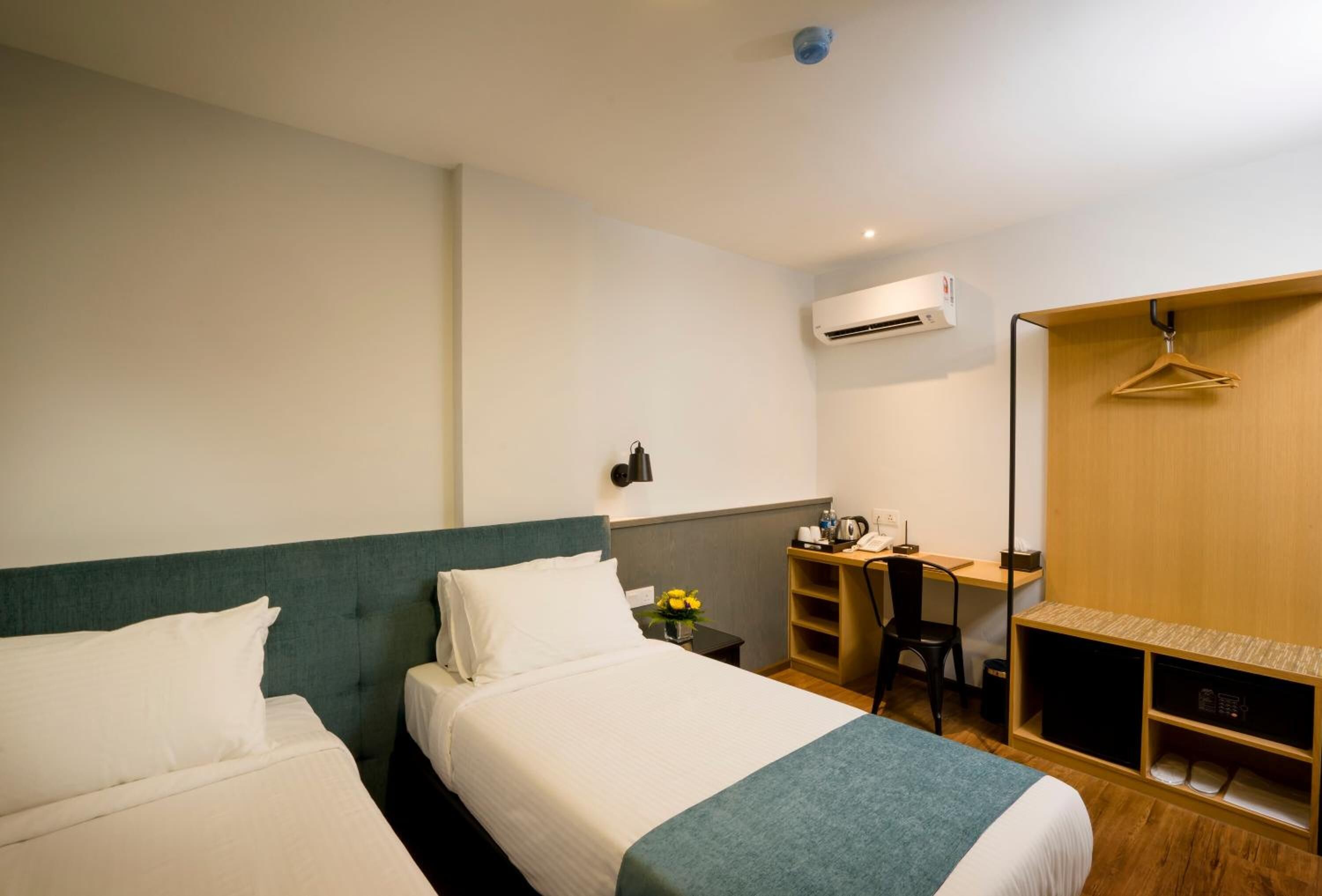 A hotel room with two beds, a desk, a chair, a wardrobe, and an air conditioning unit.