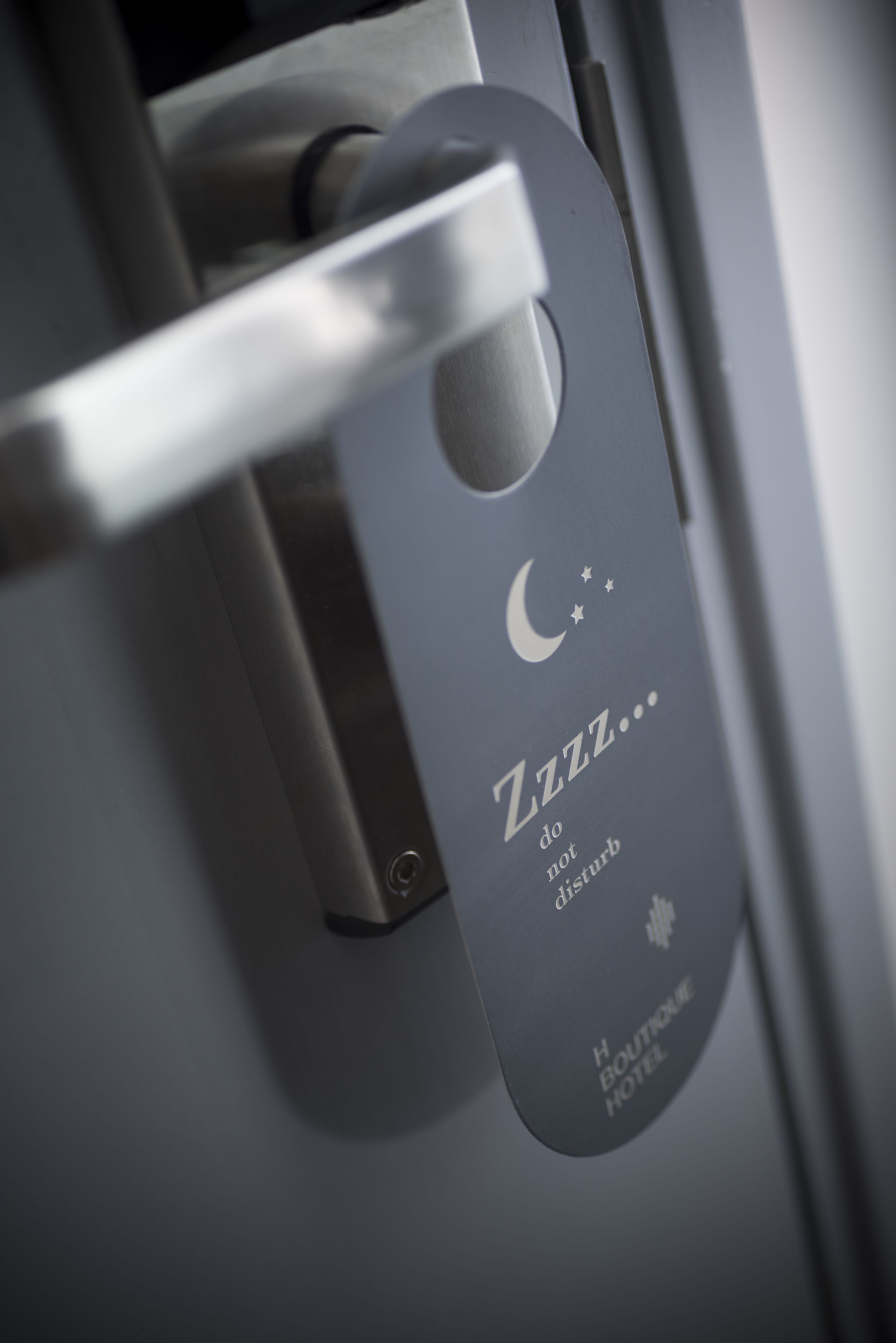 A door handle with a sign that reads "Zzz... do not disturb" and the name "H Boutique Hotel".