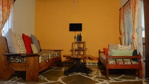 A living room with a sofa, a wooden coffee table, and a TV mounted on the wall. - Ritam Getaways (Tiwi)