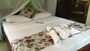 A neatly made bed with a floral bedspread, white pillows, and a rolled white towel on the side. - Ritam Getaways (Tiwi)