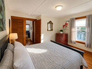 A bedroom with a bed, a dresser, a mirror, and a window with curtains.