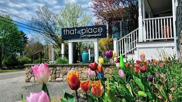 A building with a sign reading 'that place in ogonguit' and a porch with a stone wall and a garden with tulips.