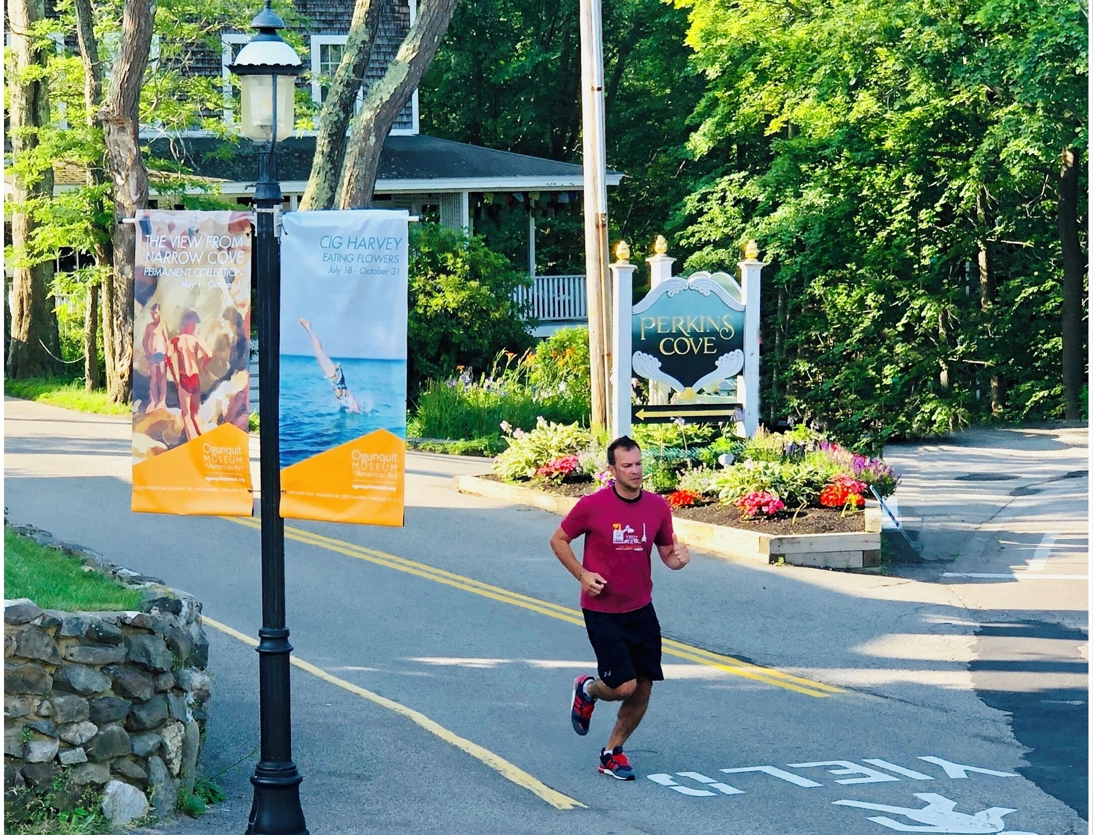 Un coureur sur une route, avec un panneau indiquant la direction de Perkins Cove et une affiche pour le musée d’Opunjait.