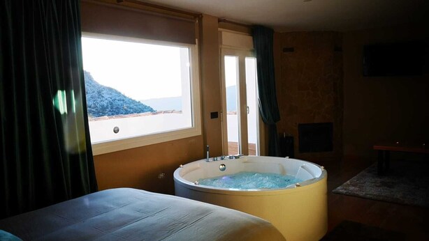 A room with a large bathtub, a bed, and a view of a mountainous landscape through a window.