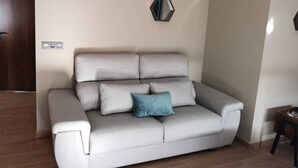 A modern living room with a grey sofa, two hexagonal mirrors on the wall, and a small wooden side table.