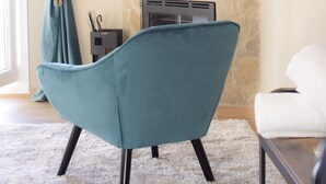 A room with a stone wall, a mounted TV, a teal armchair, and a white sofa.