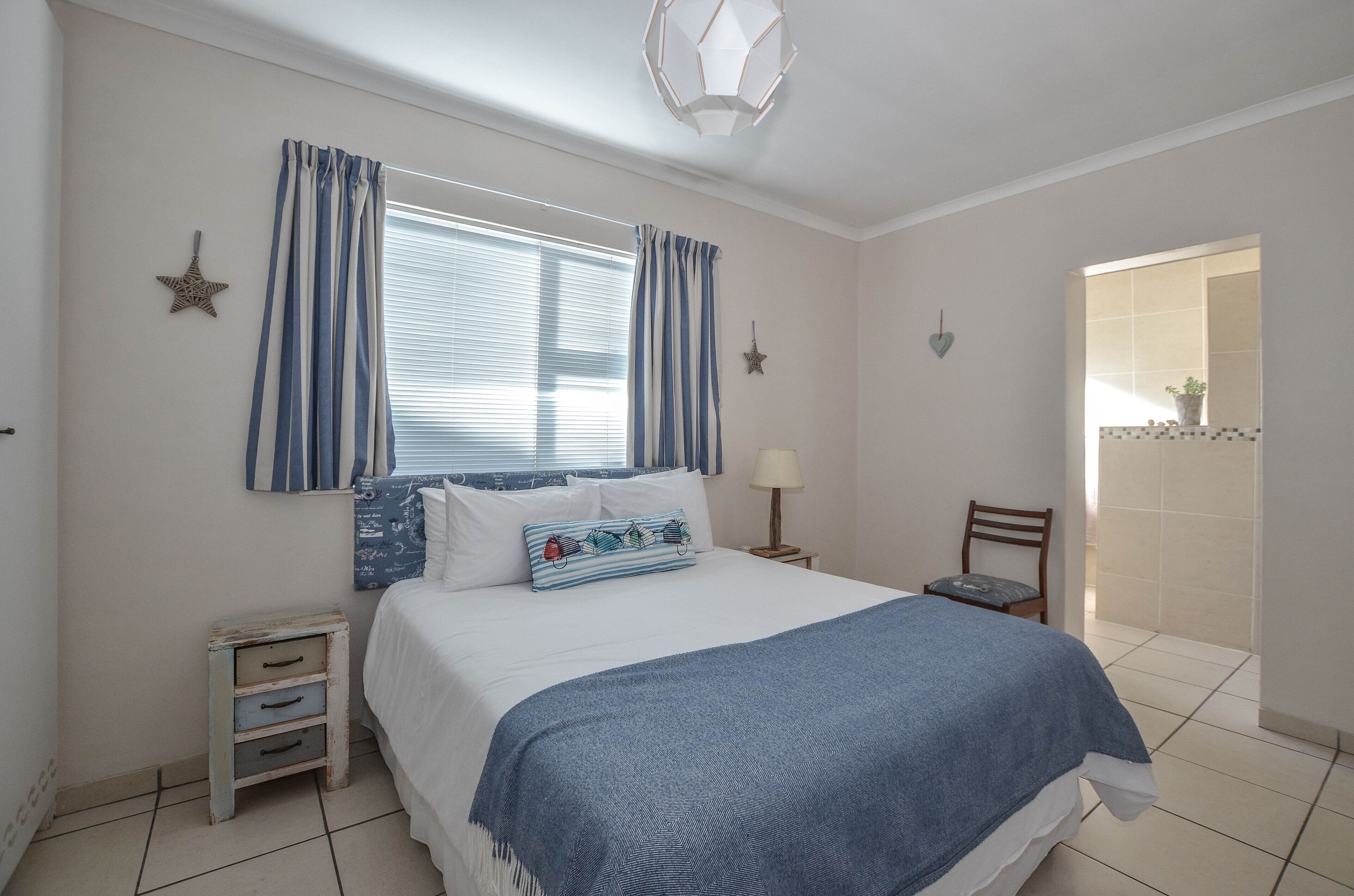 A bedroom with a bed, a nightstand, a chair, a window with curtains, and a door leading to a balcony.