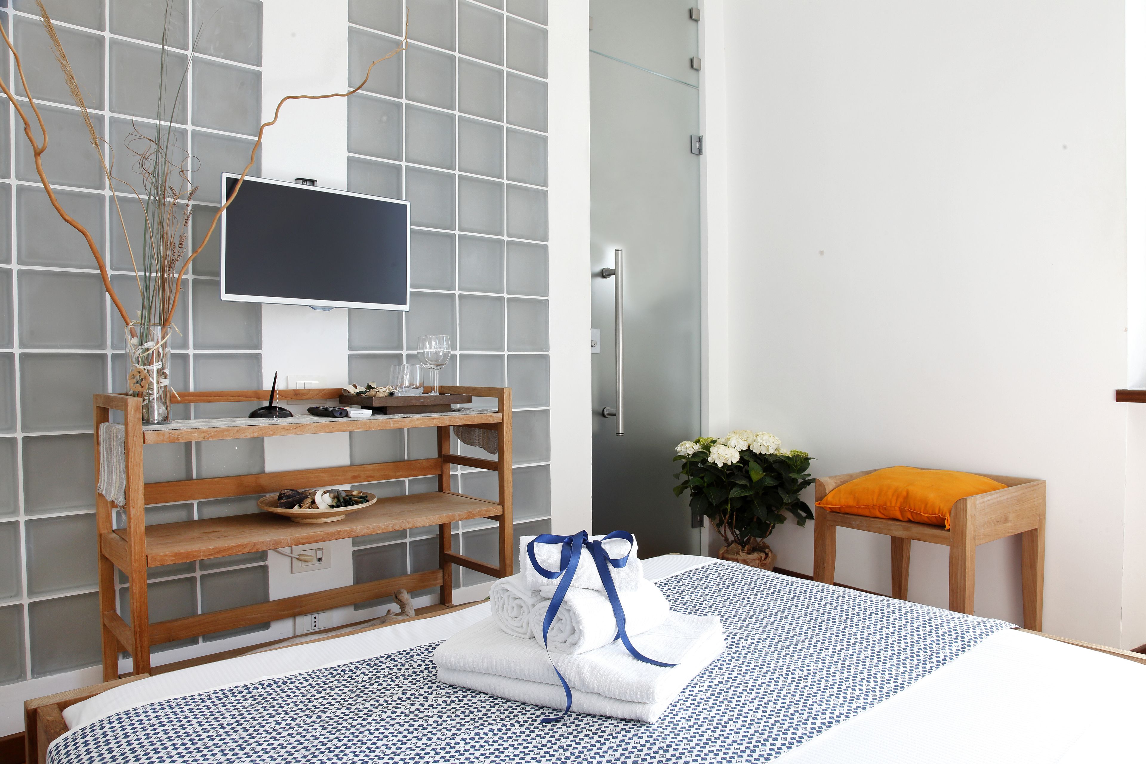 A modern hotel room with a bed, a wooden shelf with toiletries, a TV, and a shower area.