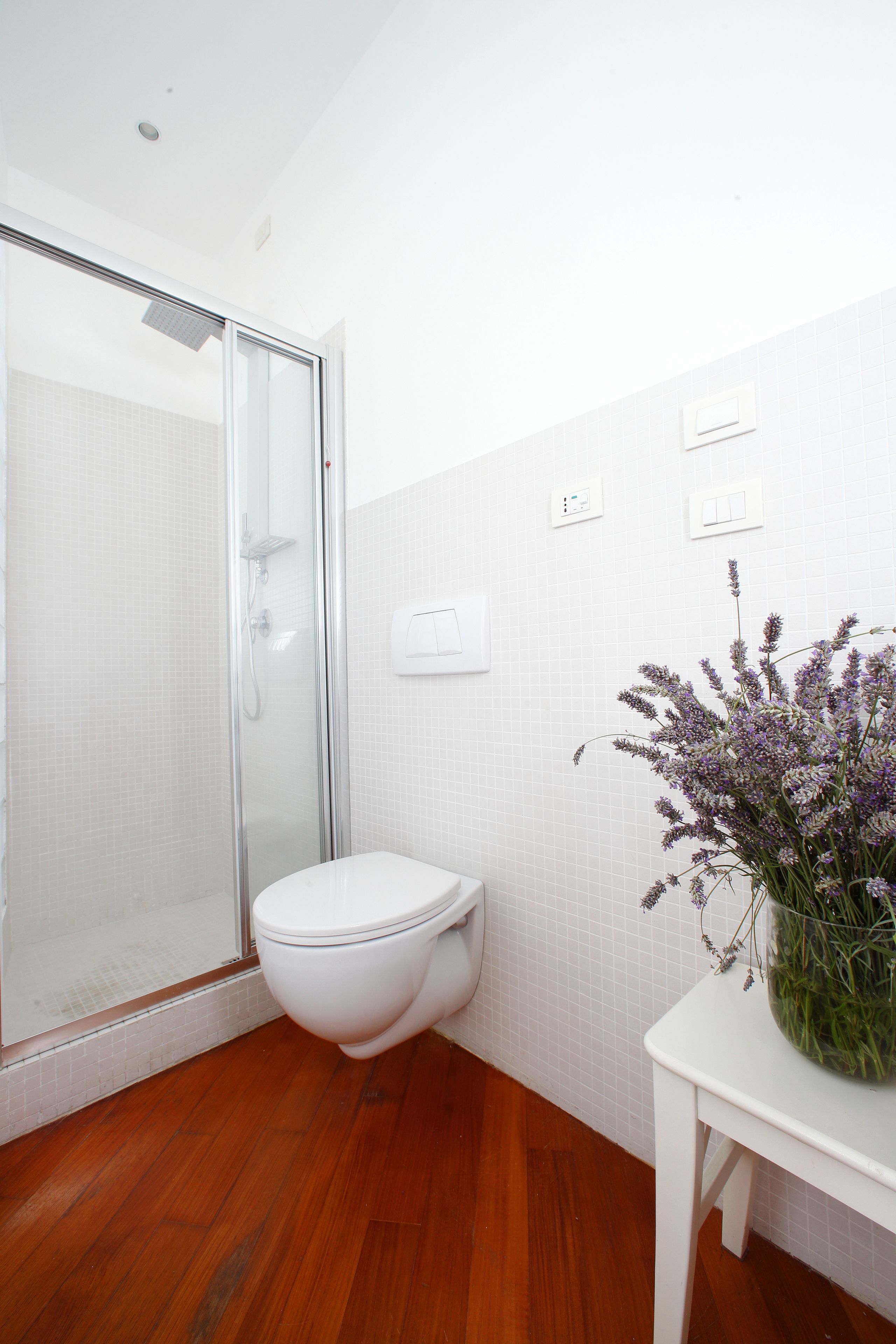A bathroom with a glass shower enclosure, a white toilet, and a white sink with a vase of flowers.