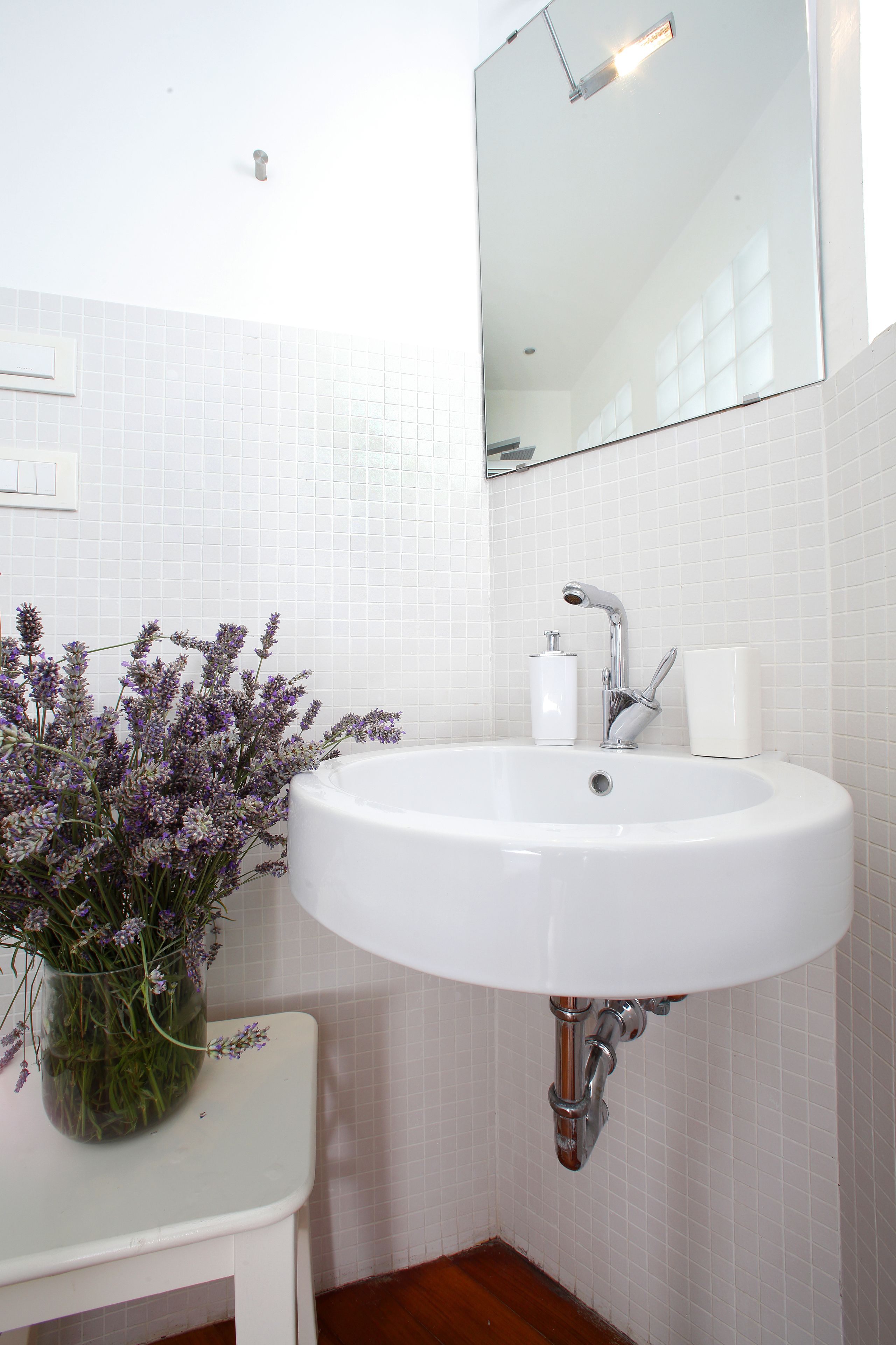 A bathroom with a white sink, a mirror, and a vase of flowers on a small table.