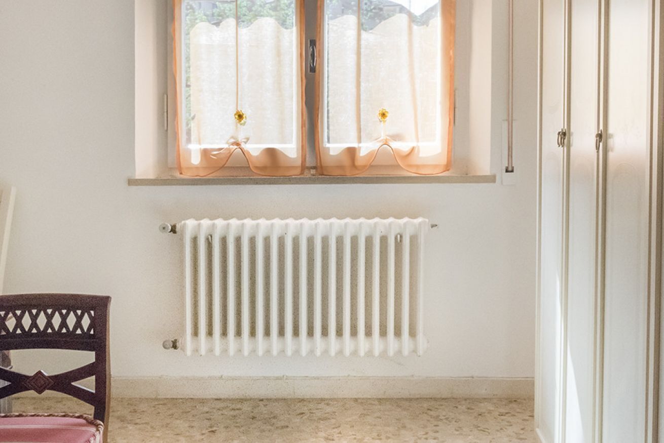 Een kamer met een radiator, een raam met gordijnen, een stoel en een kledingkast.
