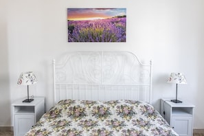 Een bed met een bloemenprint sprei, een wit metalen hoofdbord en twee nachtkastjes met lampen.
