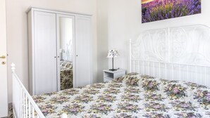 Quarto com cama, guarda-roupa, mesa de cabeceira, luminária e um quadro na parede.